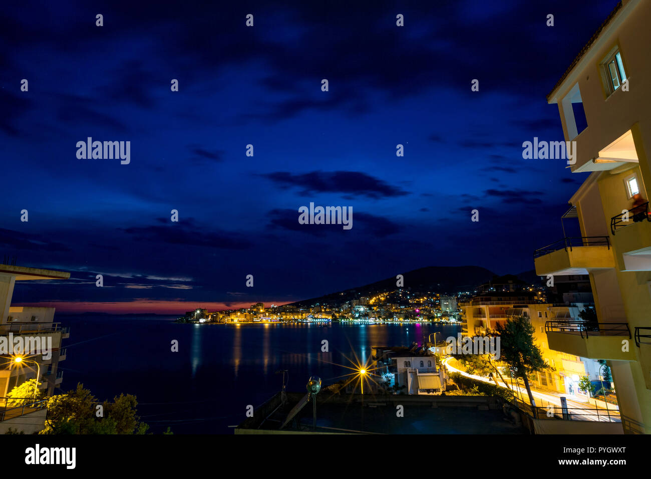Langzeitbelichtung Nacht Landschaft Foto, stadtbild am schönen Meer Stadt Saranda, Albanien mit Stern Effekt auf die Lichter der Stadt und Meer Wasser Reflexionen Stockfoto