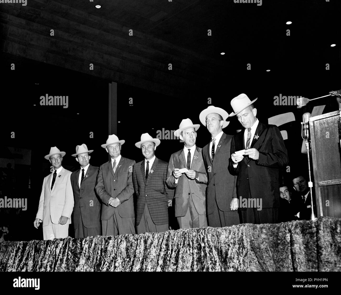 (4 Juli 1962) - - - Die ursprünglichen sieben Mercury Astronauten, jedem tragen Neue cowboyhüte und ein Abzeichen in der Form eines Sterns, abgebildet auf der Bühne an der Sam Houston Coliseum. Eine große Menschenmenge war an Hand sie zu Houston, Texas begrüßen zu dürfen. Zu recht sind Astronauten M. Scott Carpenter, L. Gordon Cooper jr., John Glenn Jr., Virgil Grissom, Walter I. M. Schirra jr., Alan B. Shepard, Jr., und Donald K. Slayton verlassen. Senator John Tower (R-Texas) ist ganz rechts im Hintergrund zu sehen. Stockfoto