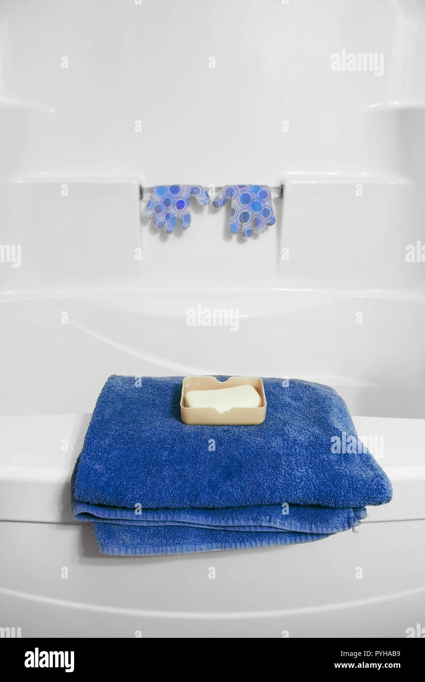 Auf dem Rand der Badewanne gibt es ein blaues gefaltetes Handtuch. Ein wenig weiter, haben wir ein paar der Exfoliation Handschuhe für den Körper sehen. Stockfoto