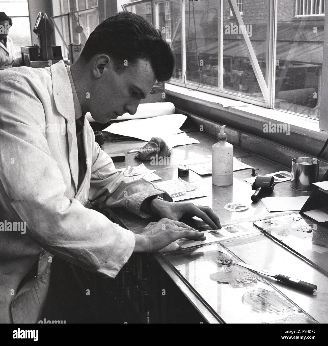 1950, historische, eine männliche Forscher in einem weißen Mantel an einer Werkbank durch ein Fenster Mischen kleiner Proben von Lack, MK malt, England, UK. Stockfoto