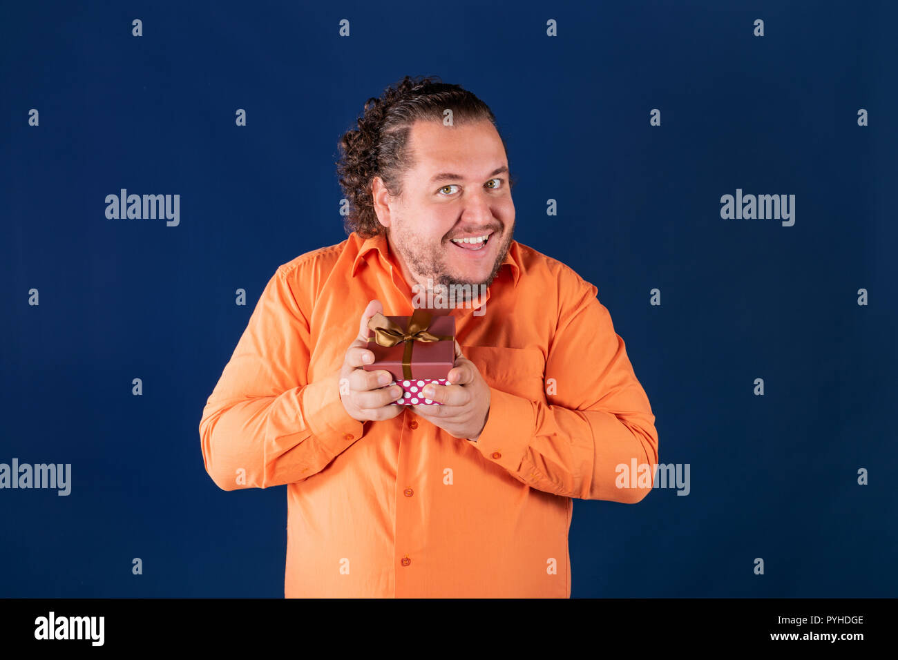 Funny fat man in orangefarbenen T-Shirt öffnet sich eine Box mit einem Geschenk Stockfoto