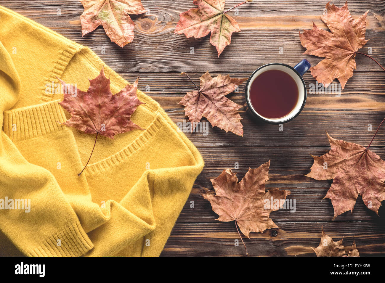 Herbst Mode saisonale Konzept, gelb Warme weiche, bequeme Pullover Strickjacke Tasse heißer schwarzer Tee Kaffee Fallen gefallen Ahornblätter auf hölzernen Tisch flach Stockfoto