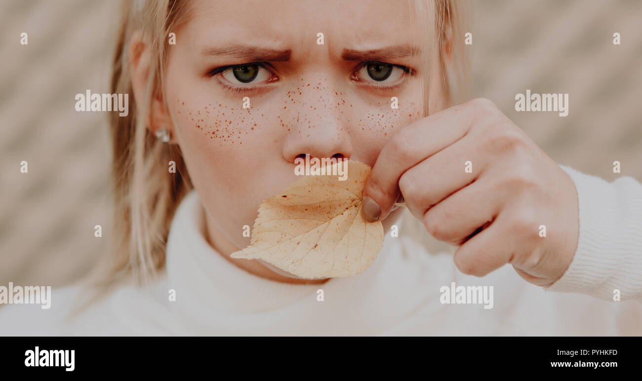 Junge Frau mit Sommersprossen in ihrem Gesicht runzelte die Stirn und die Abdeckung der Mund mit einem Blatt Stockfoto