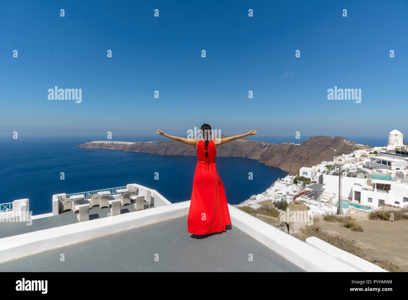Eine Frau in einem roten Kleid genießen die Imerovigli auf Santorin Kykladen Griechenland Aussicht auf einen sonnigen Sommer am Nachmittag Stockfoto