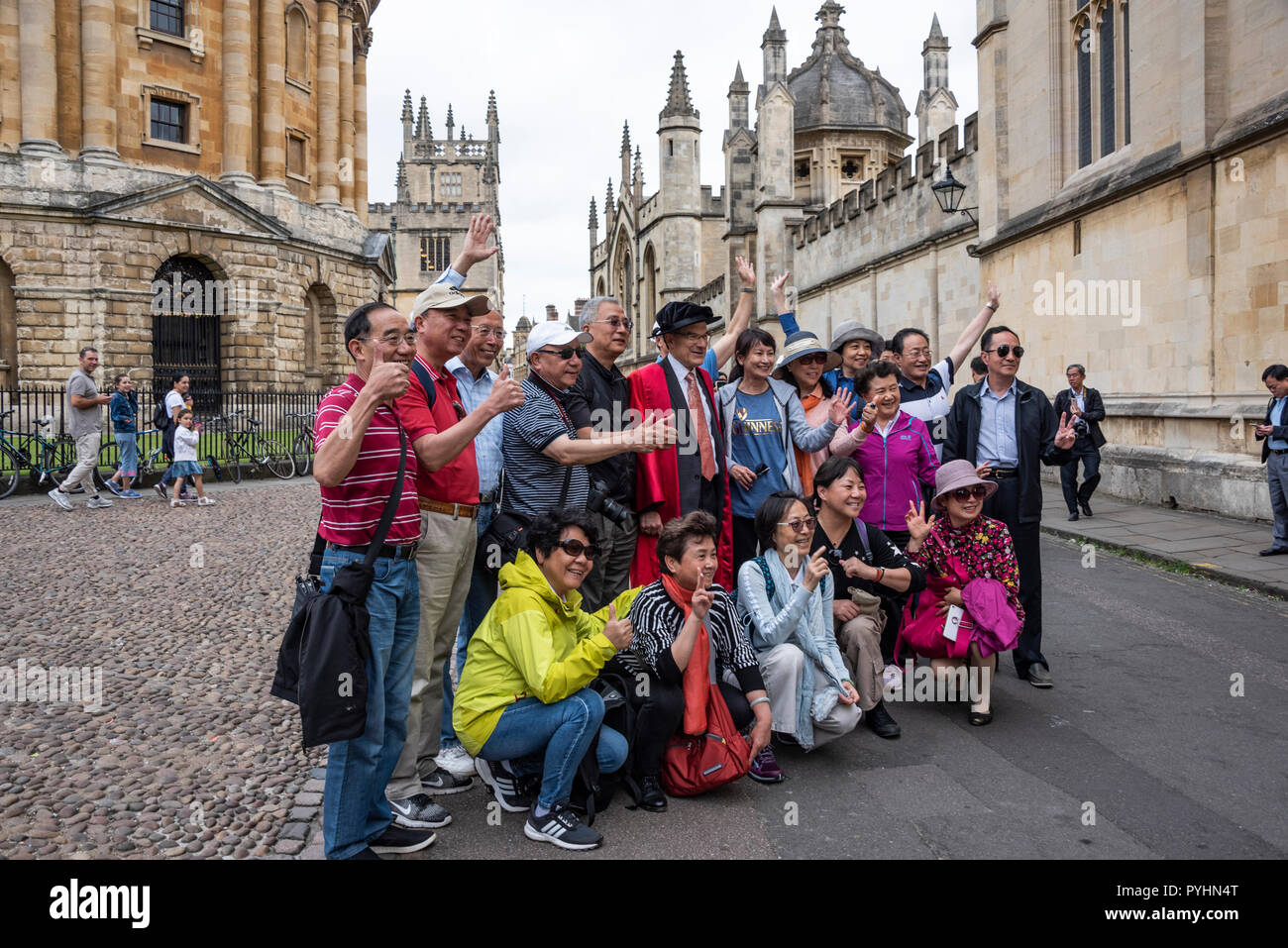 Eine Gruppe von asiatischen Touristen posieren für ein Foto mit einem Teilnehmer des Encaenia Zeremonie, Oxford, Großbritannien Stockfoto