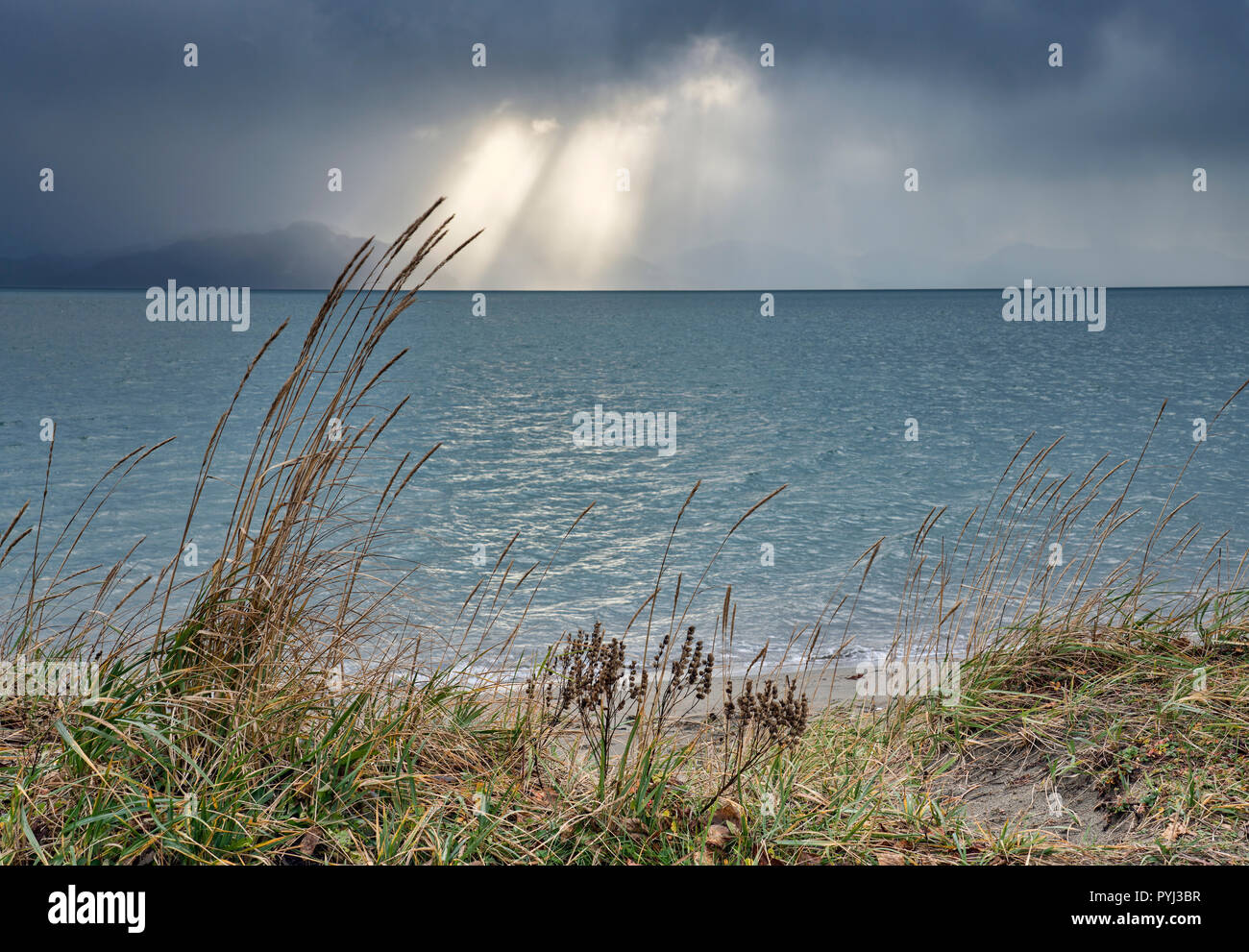 Sonnenstrahlen brechen durch schwere Gewitterwolken über dem Meer auf einem Strand in Südostalaska. Stockfoto