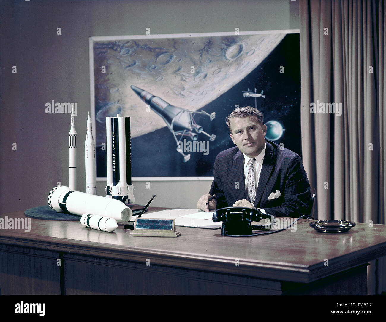 Foto des Marshall Space Flight Center (LINKS) Geschäftsführer Dr. Wernher von Braun an seinem Schreibtisch mit Moon Lander im Hintergrund und Rakete Modelle auf seinem Schreibtisch. Stockfoto