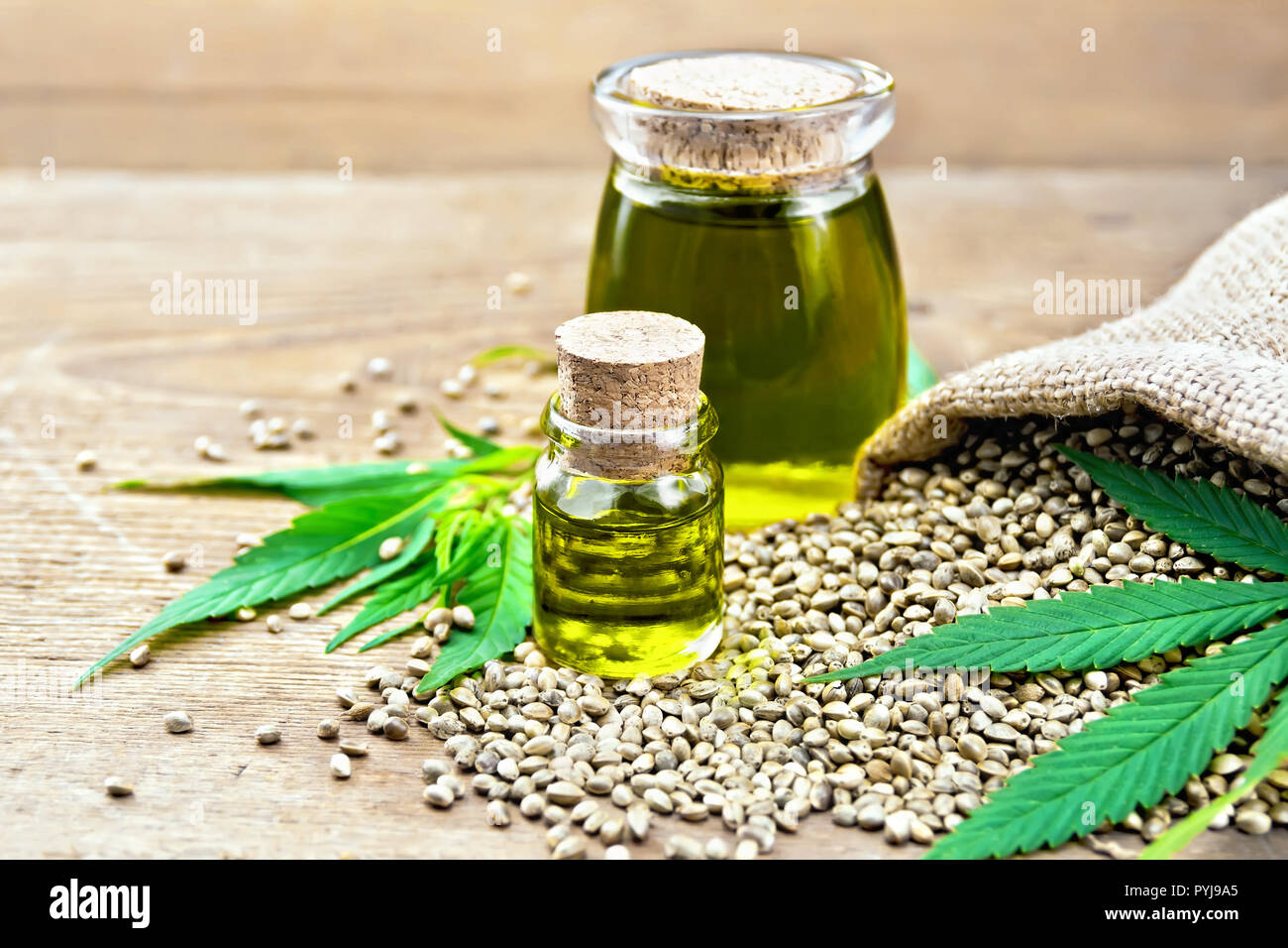 Hanf Öl in zwei Gläser mit Getreide im Sack, Blätter und Stängel von Cannabis auf dem Hintergrund der alten hölzernen Brettern Stockfoto