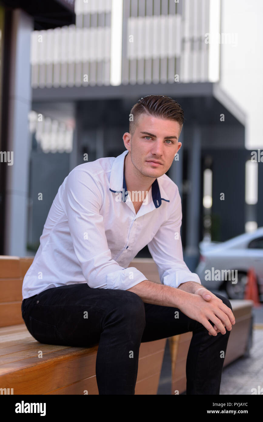 Jungen gutaussehenden Mann sitzen draußen und Suchen an Kamera Stockfoto