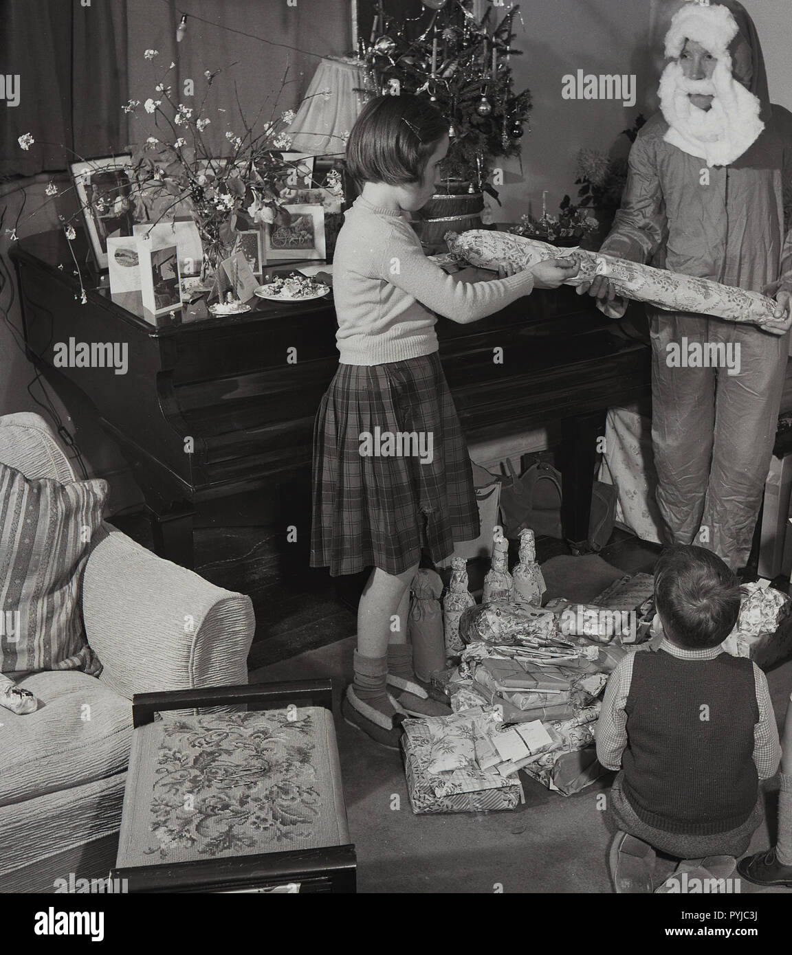 1950, historische, in einem Zimmer vorne, beisde ein Klavier, ein junges Mädchen, ein Geschenk von ihrem Vater in ein Kostüm als Weihnachtsmann, England, UK gekleidet. Stockfoto