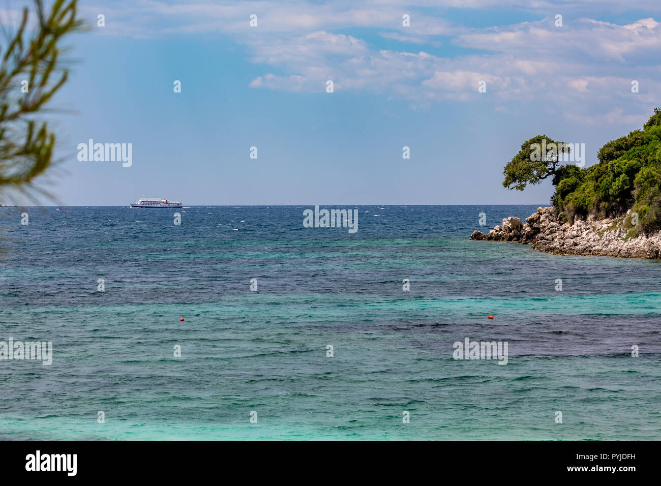 Feder tagsüber schönen Ionischen Meer mit klaren türkisfarbenen Wasser, Felsen und Bäume Küste Blick von Ksamil Strand, Albanien. Tief blauen Himmel mit weißen Wolken. Stockfoto