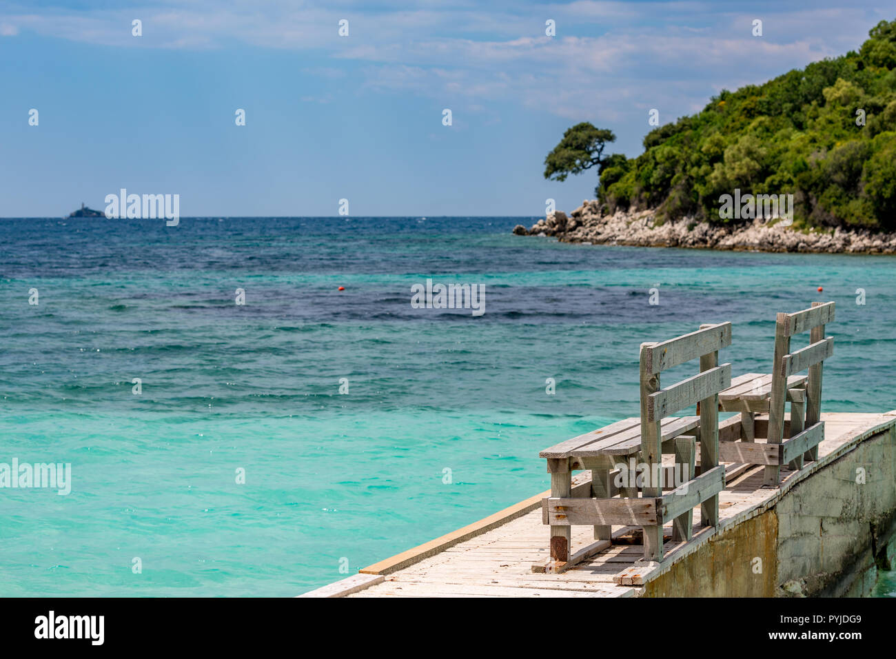 Feder tagsüber schönen Ionischen Meer mit klarem, türkisfarbenem Wasser, Holz- pier und feinen Sand der Küste Blick von Ksamil Strand, Albanien. Tief blauen Himmel mit weißen Wolken. Stockfoto