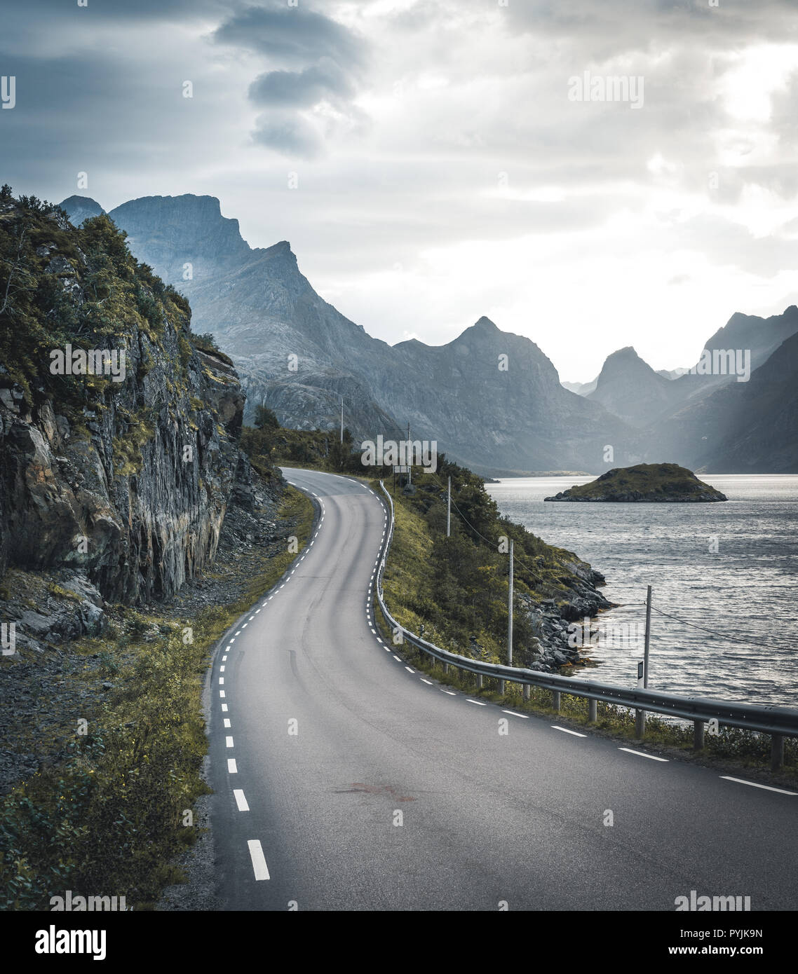 Kurvenreiche Straße Reise in Richtung Henningsvær auf den Lofoten Inseln mit Bergen im Hintergrund. Bewölkt und Moody Himmel mit Atlantik. Foto in N genommen Stockfoto