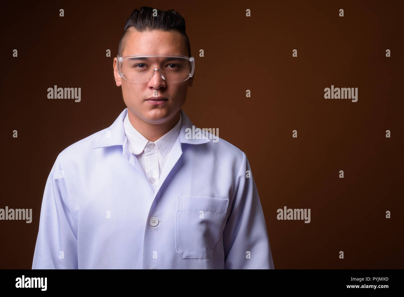 Junge schöne multi-ethnischen Mann Arzt gegen braunen Hintergrund Stockfoto