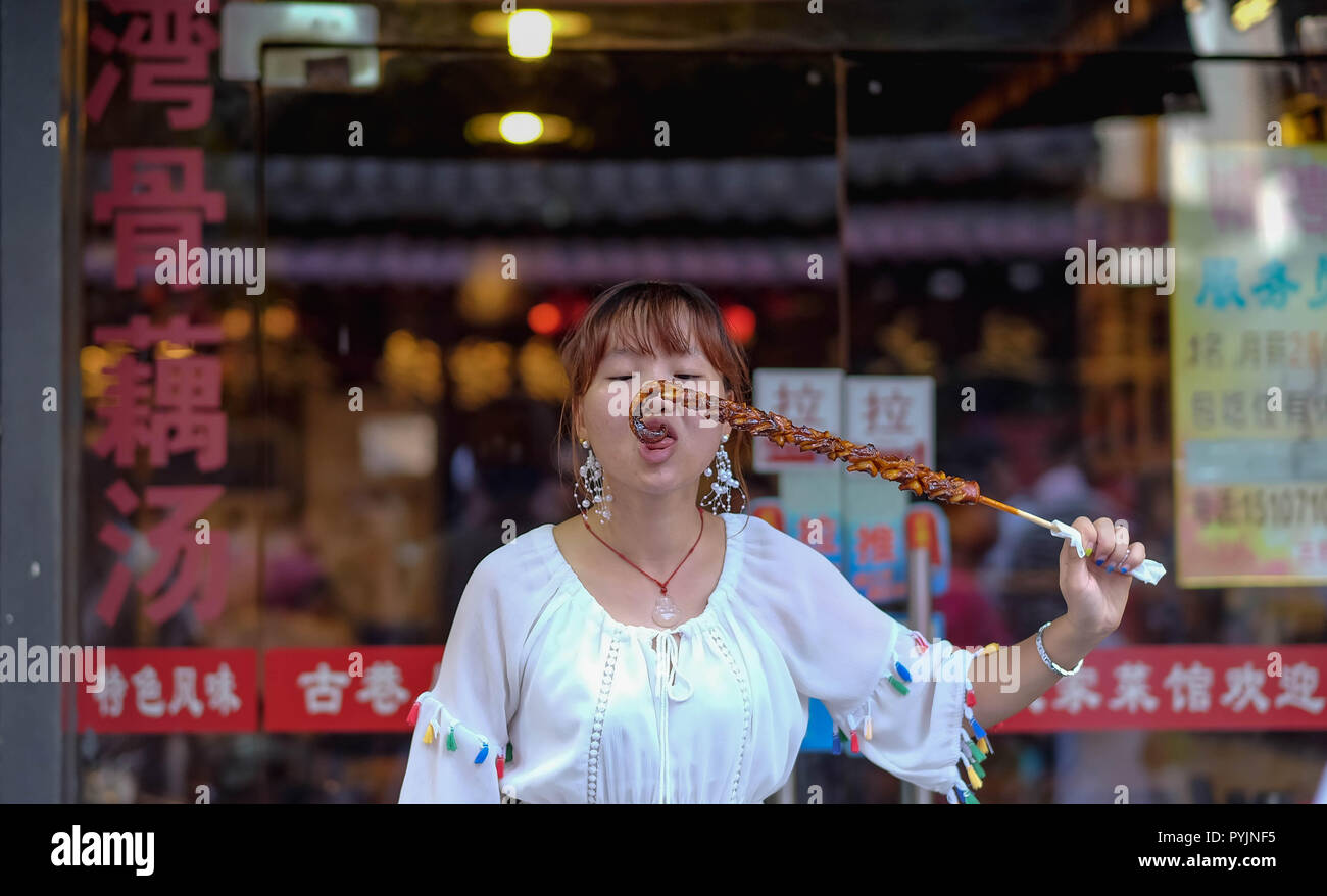 WUHAN CHINA - September 8, 2018: eine Frau ist eatting der squid-Grill an der Straße essen, Hubuxiang Street, Provinz Hubei. Stockfoto