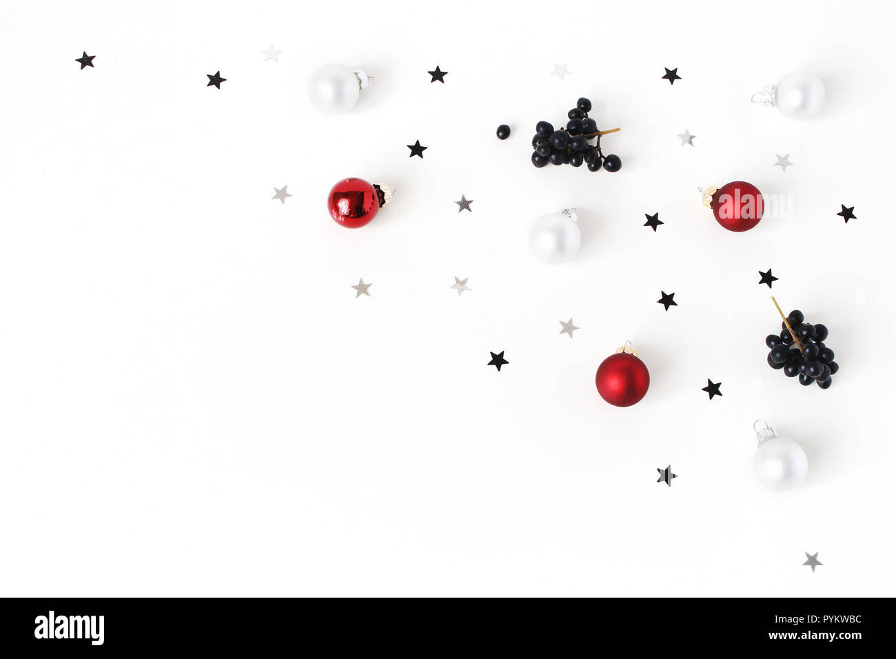 Weihnachten Komposition. Rote und weiße Weihnachten Kugeln aus Glas, Flitter, Konfetti Sterne silber und schwarz, Liguster Ligustrum Beeren auf weißem Hintergrund. Flach, Ansicht von oben. Dekorative winter Muster. Stockfoto