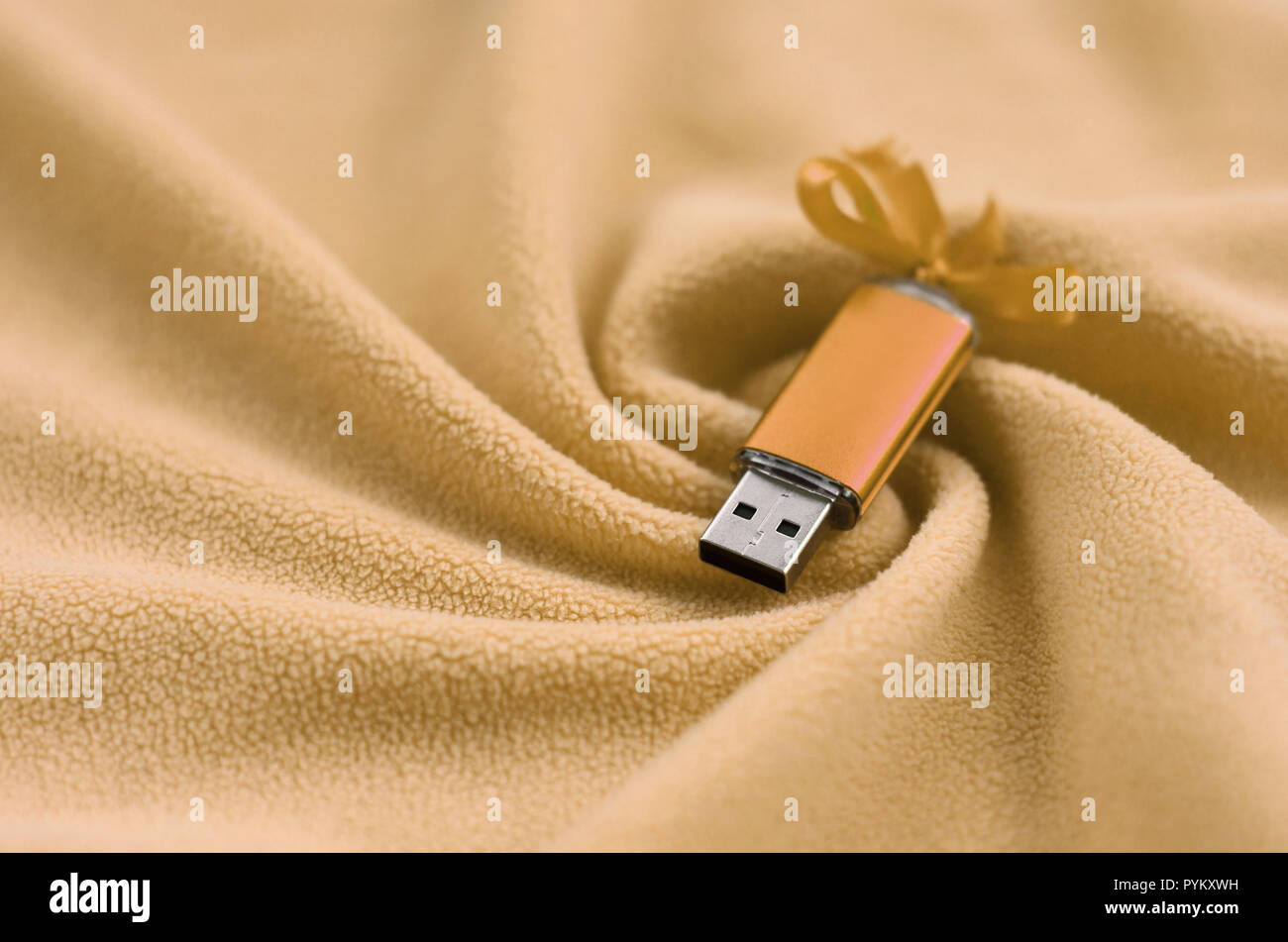 Orange usb Flash Memory Card mit einem Bogen liegt auf einer Decke aus weichem und haarige Licht orange Fleece Stoff mit viel Entlastung falten. Speicher Devi Stockfoto