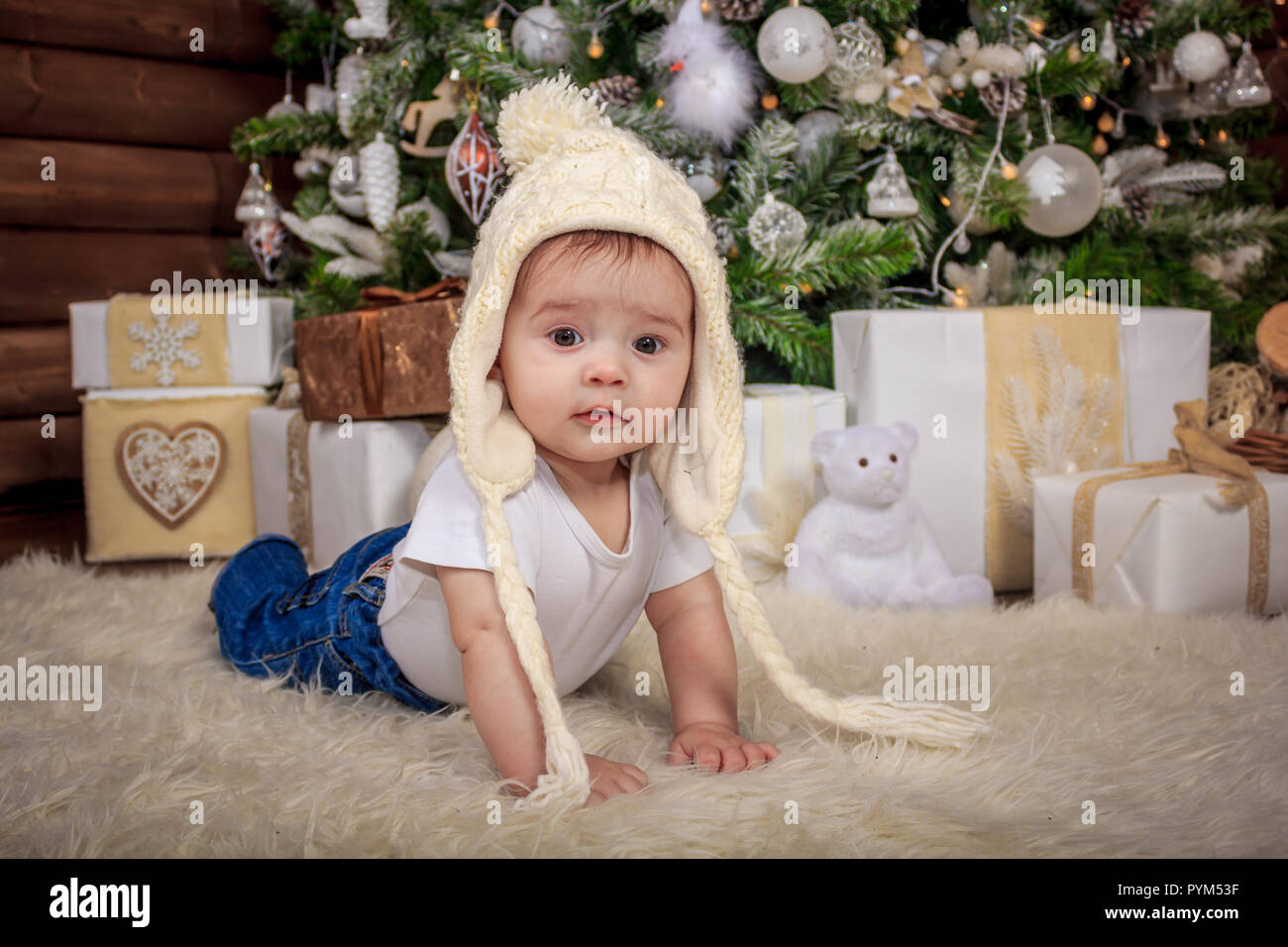 Baby in elf Kostüm spielen mit alten hölzernen Zug und Stofftier Bären unter den Weihnachtsbaum, vintage. Das Baby in die Gap liegt unter dem Baum und sm Stockfoto