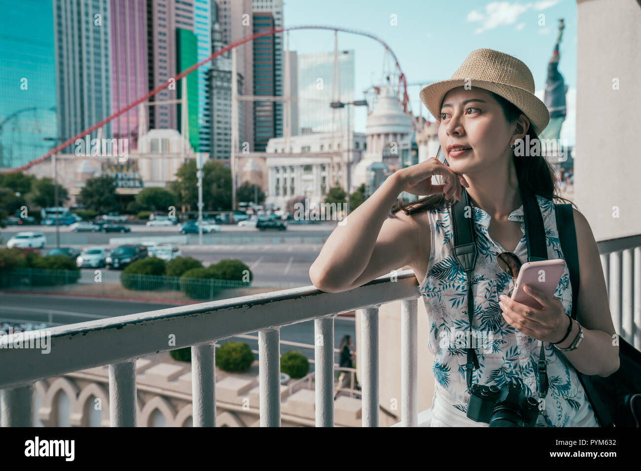 Touristische Frau mit Online Ratgeber auf dem Mobiltelefon unter Berufung auf den Handlauf in Gang. Genießen der städtischen Ansicht im sonnigen Tag. Reisen in den USA. Stockfoto