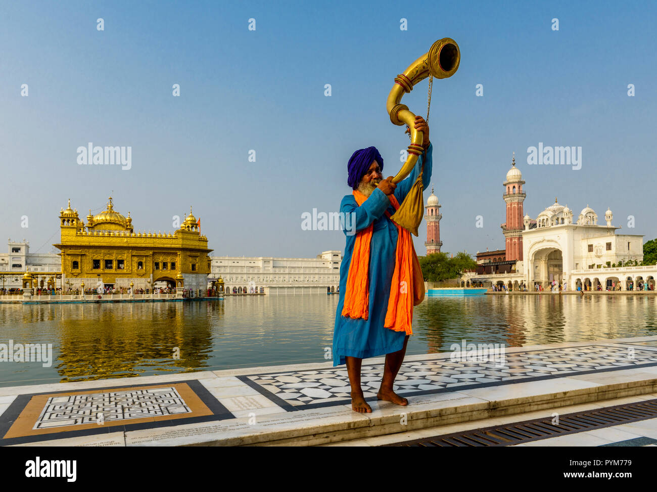 Ein nihang, einem Sikh heiliger Mann, steht und Blasen eine große Messing Horn an der heiligen Pool der Harmandir Sahib, der Goldene Tempel Stockfoto