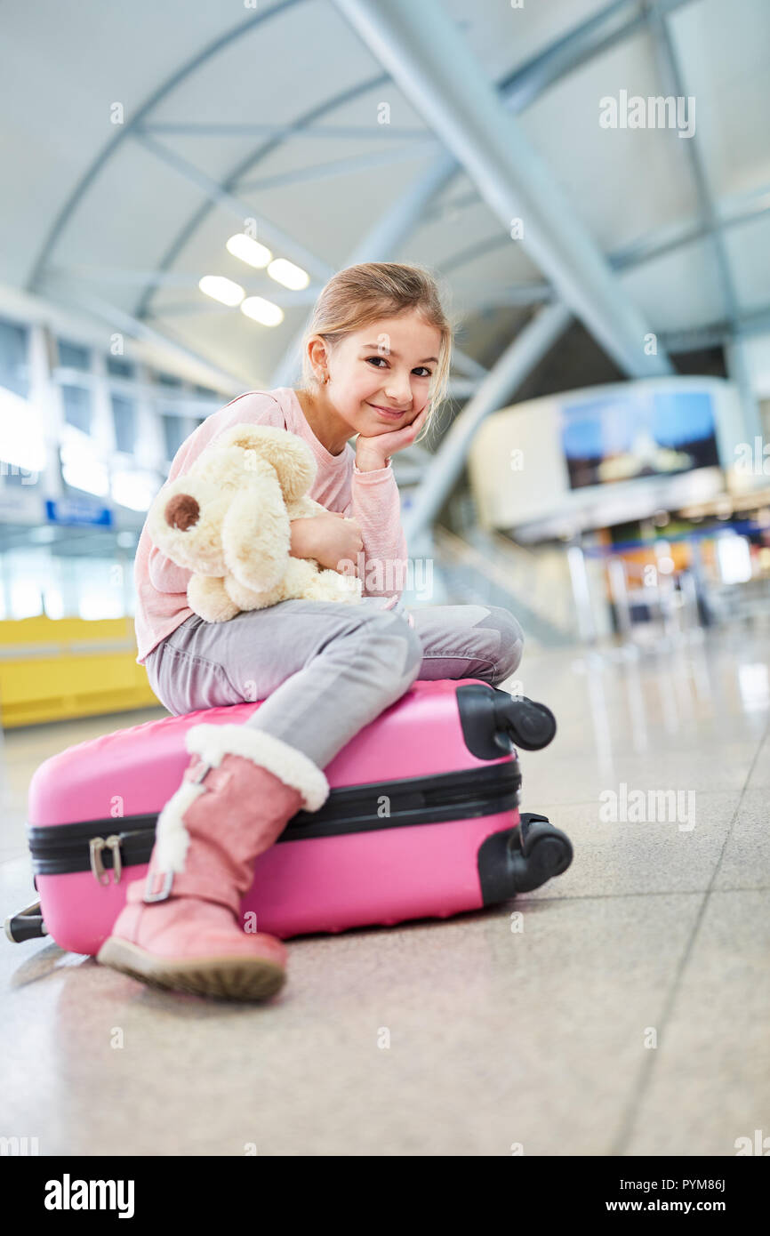 Kleines Mädchen mit Stofftier sitzt auf einem Koffer ist, wartet in der Ankunftshalle des Flughafens. Stockfoto