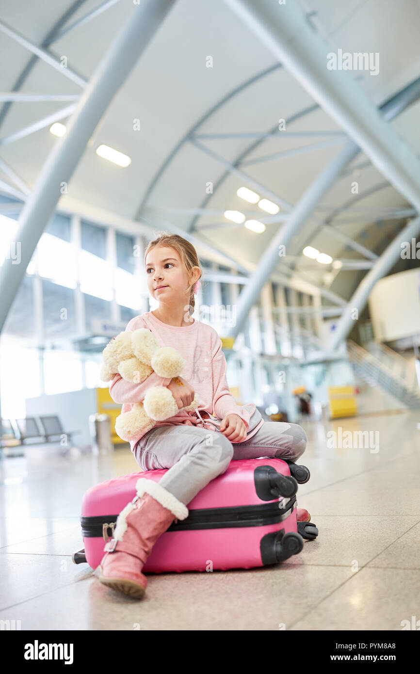 Alleinreisende Kind sitzt auf einem Koffer und wartet auf die Abfahrt in der Ankunftshalle des Flughafens. Stockfoto