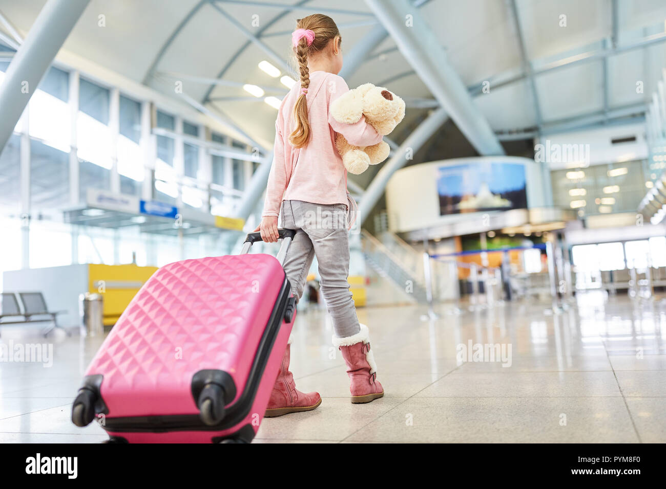 Mädchen als Passagier mit Koffer und Stofftier im Flughafenterminal reist allein Stockfoto