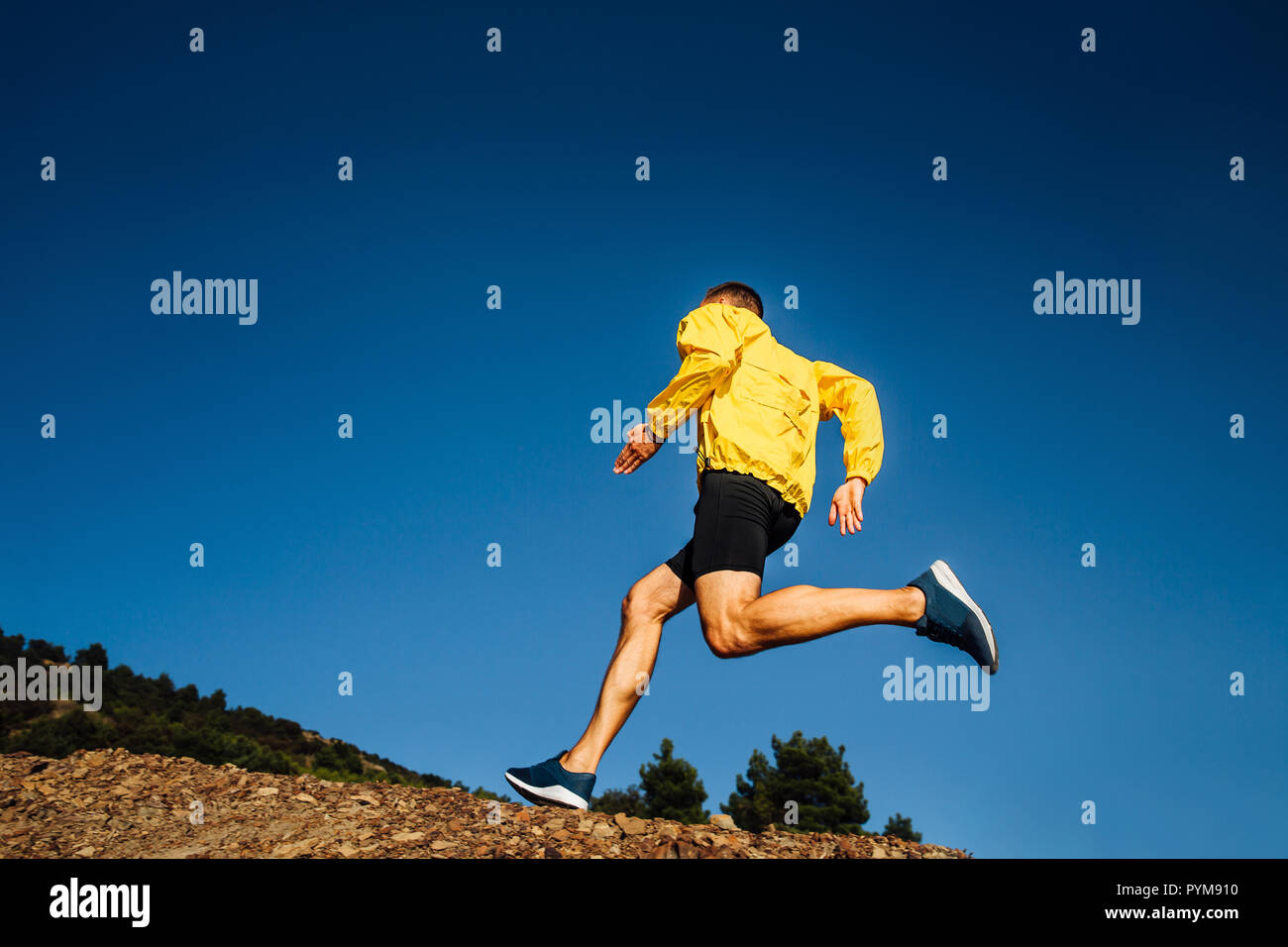 Männliche Athlet Läufer in gelber Jacke laufen bergauf Stockfoto