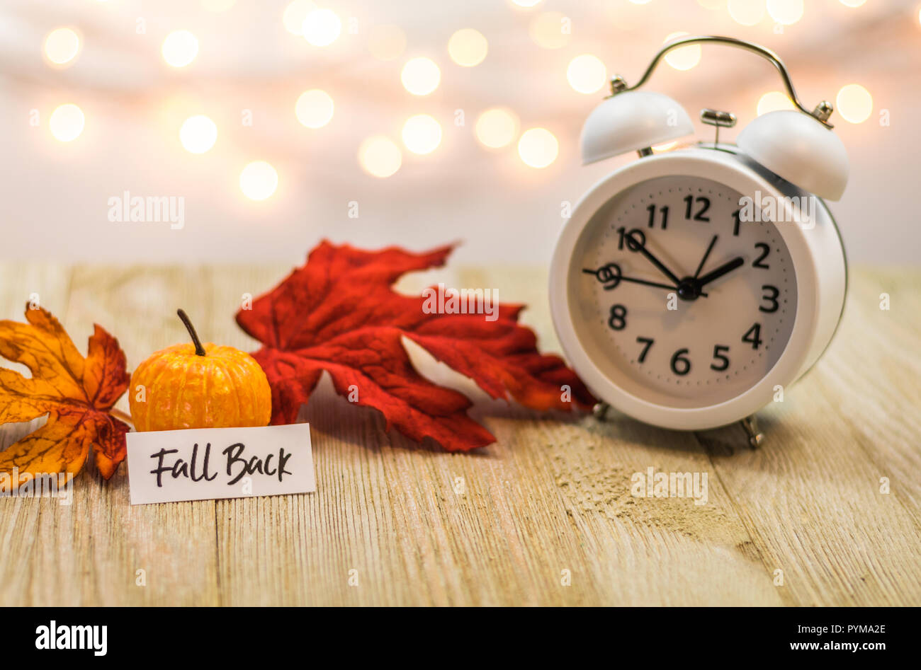 Zurück Sommerzeit Konzept mit weißen Wecker und Blätter im Herbst, weiches bokeh Hintergrund auf Holzbrett Stockfoto