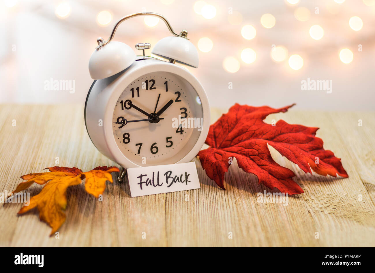 Zurück Sommerzeit Konzept mit weißen Wecker und Blätter im Herbst, weiches bokeh Hintergrund auf Holzbrett Stockfoto