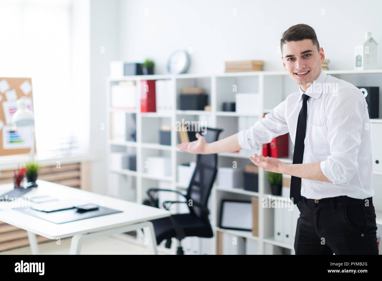 Ein junger Mann im Büro lädt Sie ein, am Tisch zu sitzen. Stockfoto