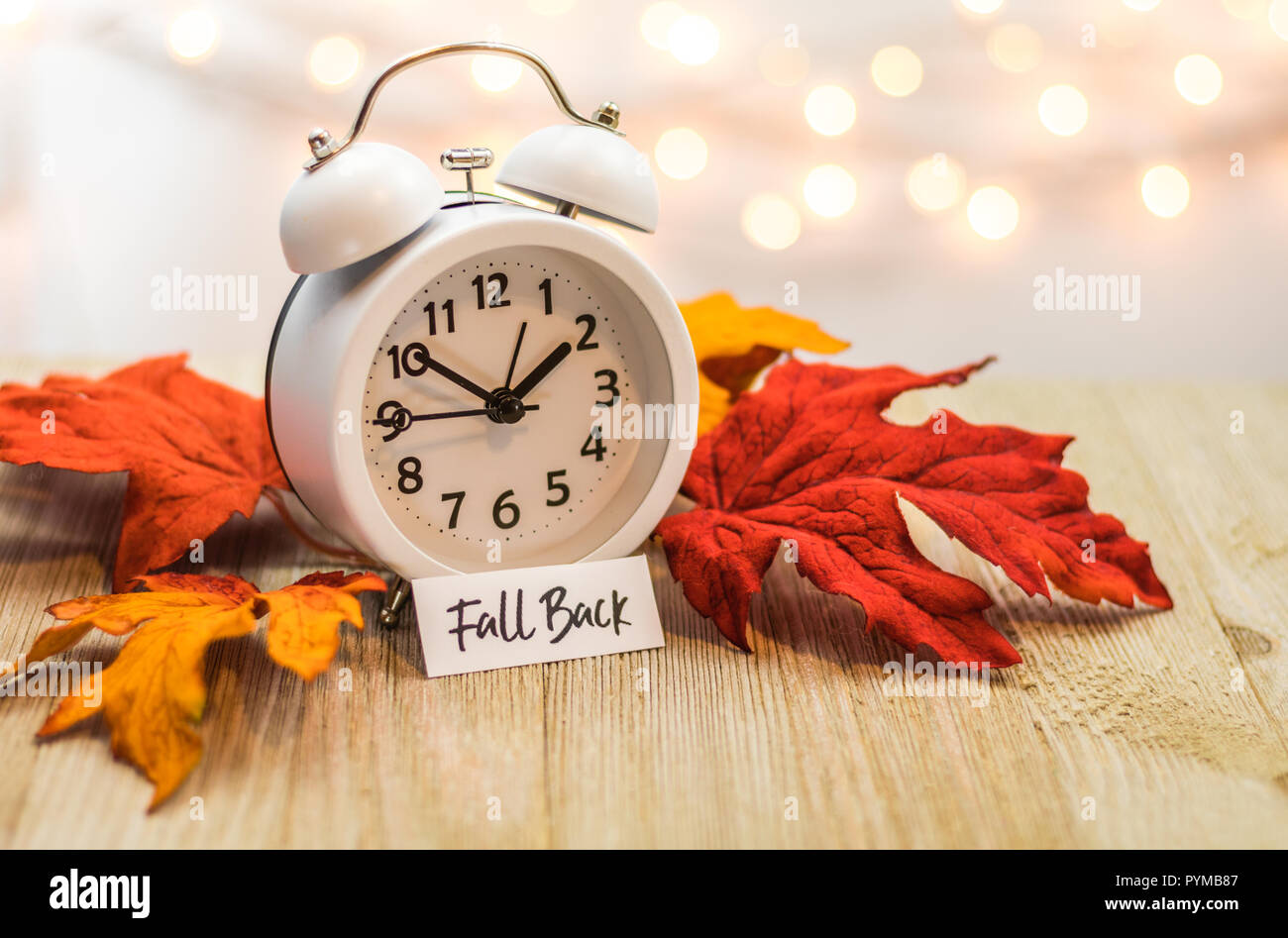 Zurück Sommerzeit Konzept mit weißen Wecker und Blätter im Herbst, weiches bokeh Hintergrund auf Holzbrett Stockfoto
