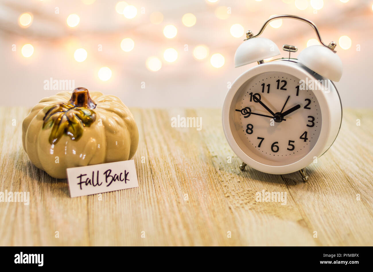 Zurück Sommerzeit Konzept mit weißen Wecker und Blätter im Herbst, weiches bokeh Hintergrund auf Holzbrett Stockfoto