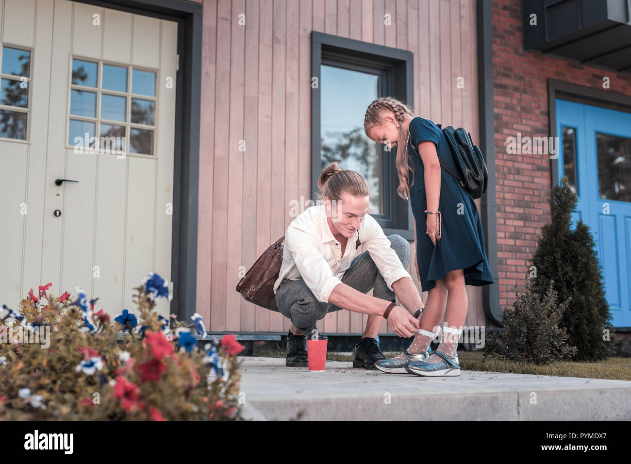 Liebevolle blonde Vater kümmert sich um sein kleines Schulmädchen in der Nähe des Hauses Stockfoto