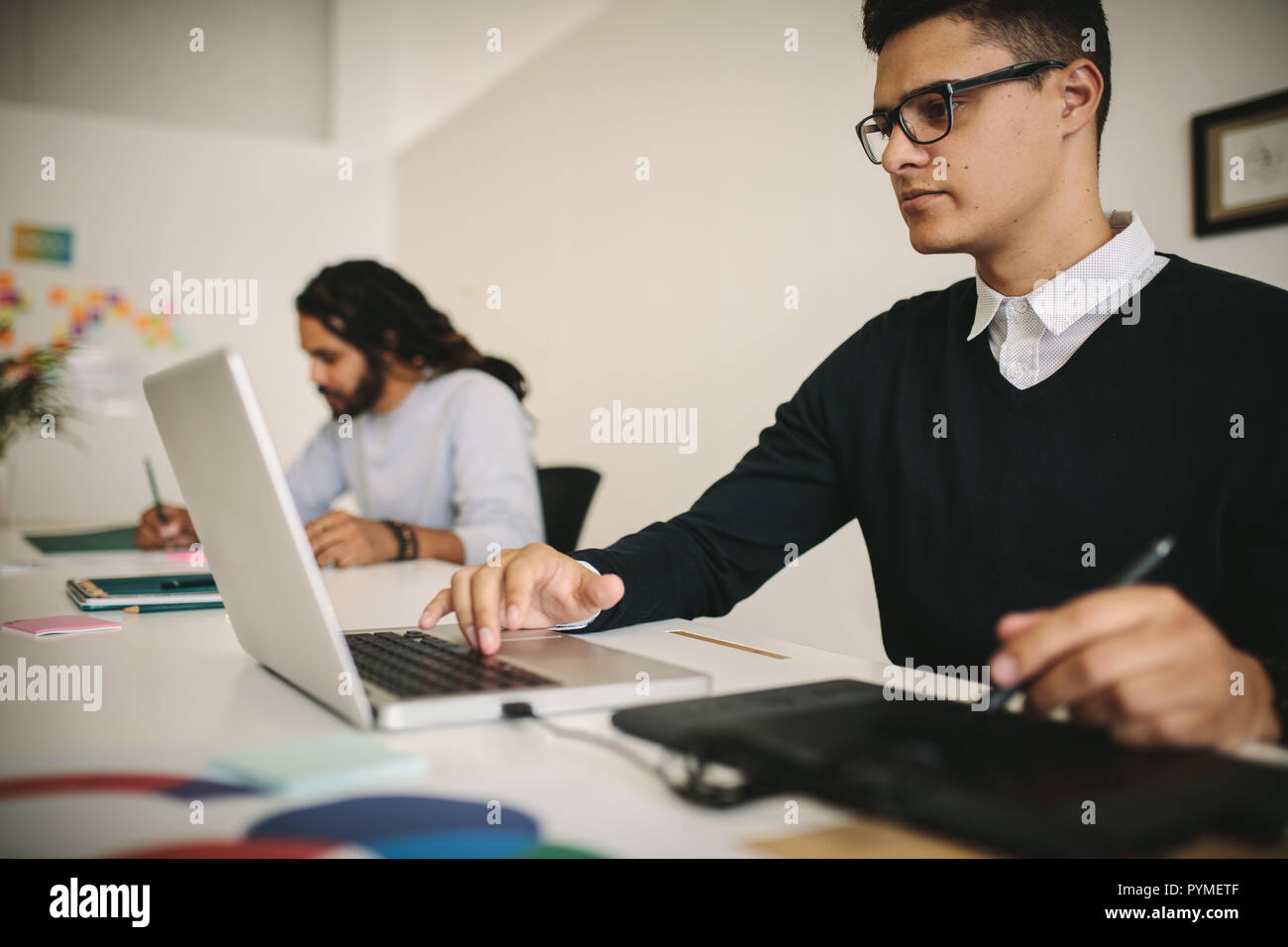 Geschäftsmann, der ein digitales Schreibpad verwendet, während er an einem Laptop arbeitet. Kreatives Geschäftsteam, das im Büro arbeitet. Stockfoto