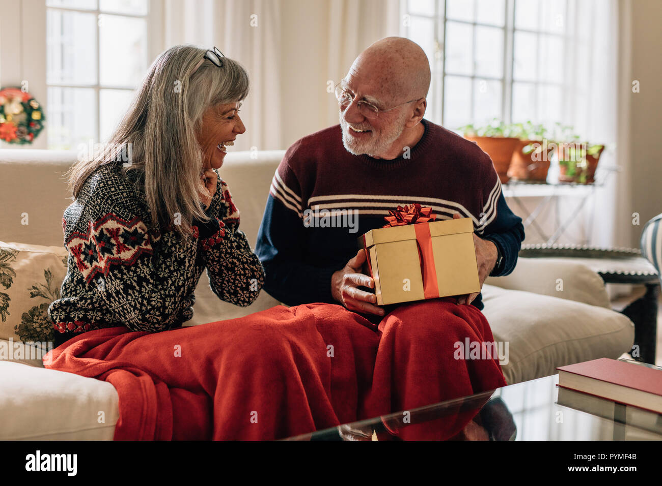 Älterer Mann, ein Weihnachtsgeschenk für seine Frau. Alter Mann saß auf der  Couch mit seiner Frau hält ein Weihnachtsgeschenk in der Hand  Stockfotografie - Alamy