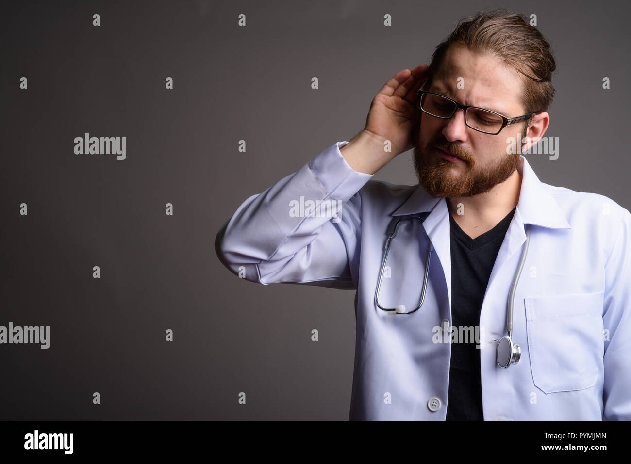 Junger bärtiger Mann Arzt gegen grauer Hintergrund Stockfoto