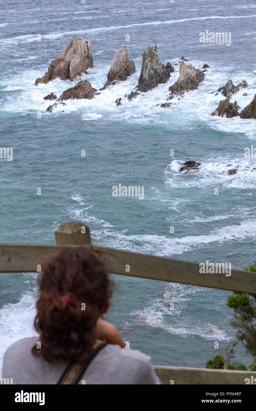 Gueirua Strand, Asturien, Spanien. Vertikale Ansicht von touristischen Frau beobachten die rauhe See brechen im Riff. Stockfoto