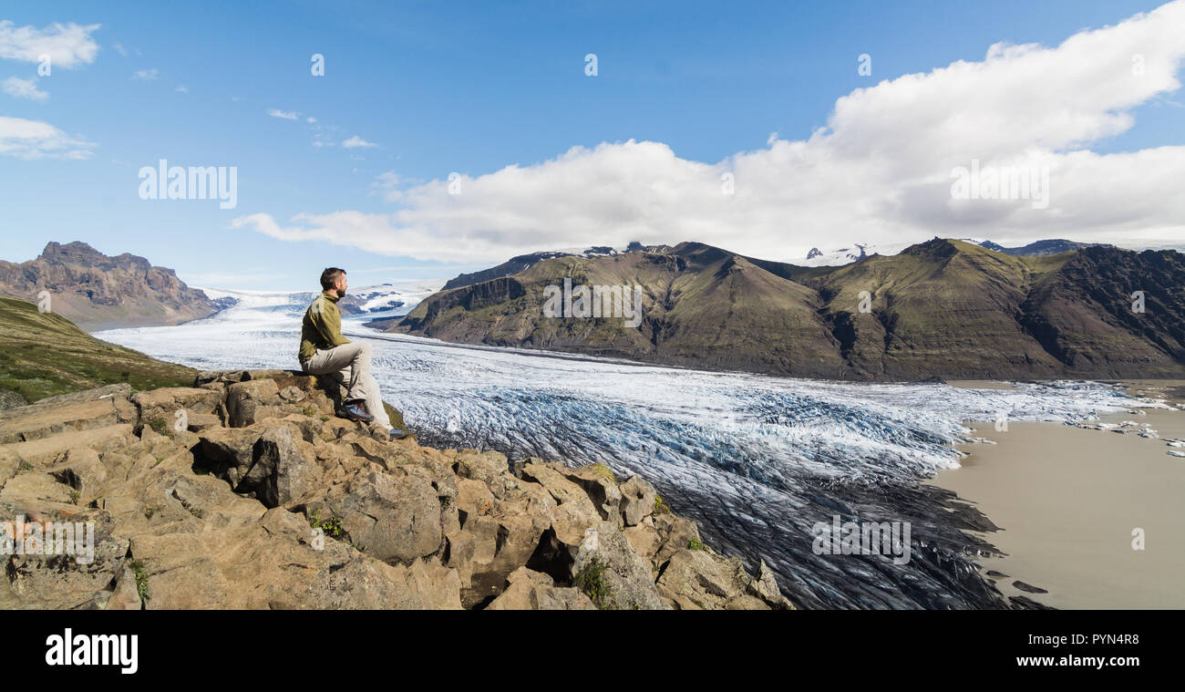 Mann sitzt auf Felsen mit Blick auf Skaftafellsjokull Teil des Vatnajökull Gletscher im Nationalpark Skaftafell, Island. Stockfoto