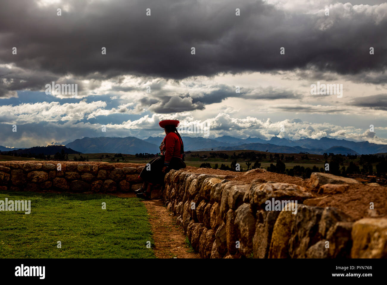 Einwohnerin des peruanischen Dorfes sitzt in Steinmauer und schaut auf den Horizont, Peru, Archäologie Stockfoto