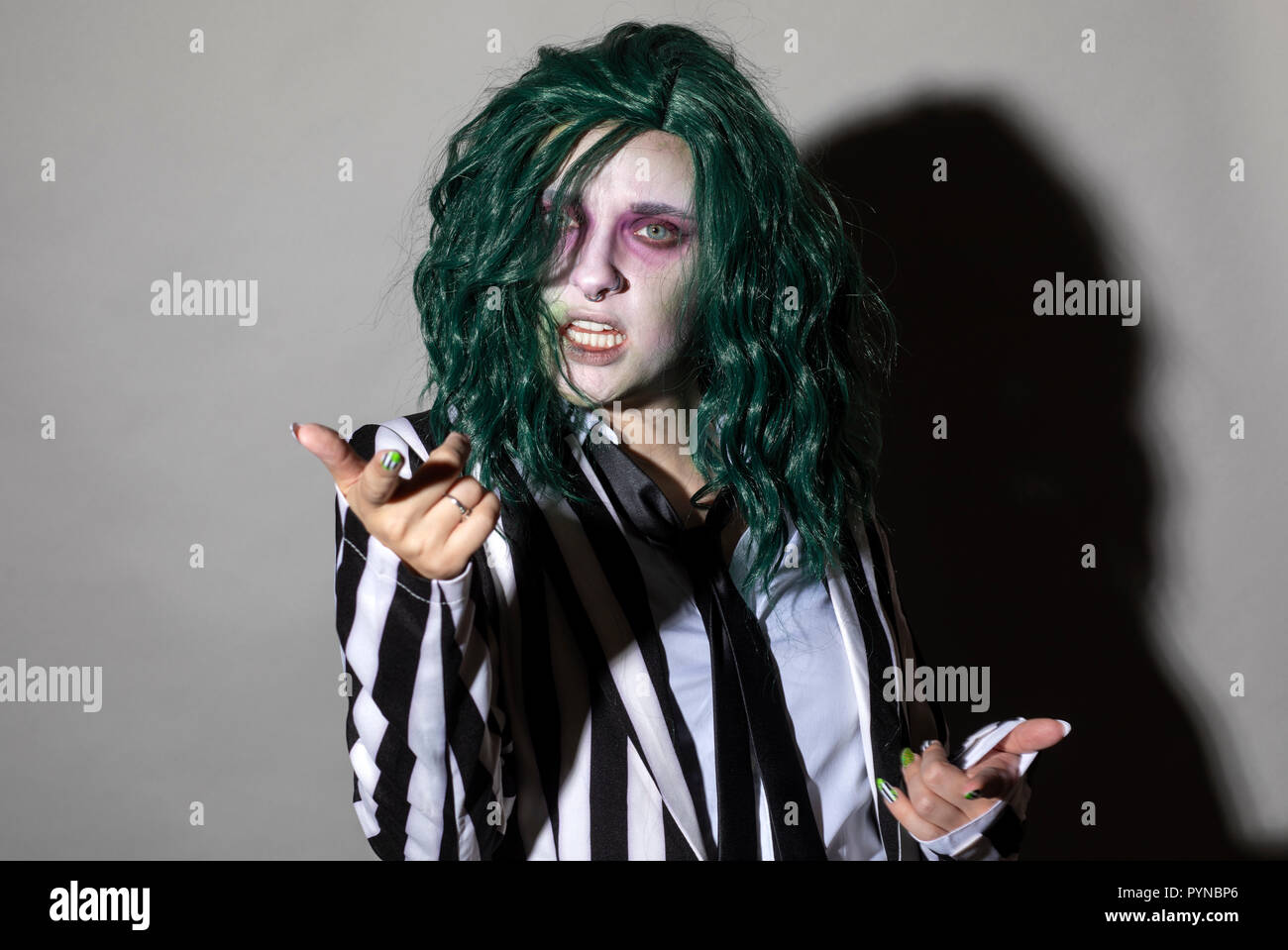 Eine junge Frau kleidet sich für Halloween im Nadelstreifenanzug und grüne Haare. Stockfoto