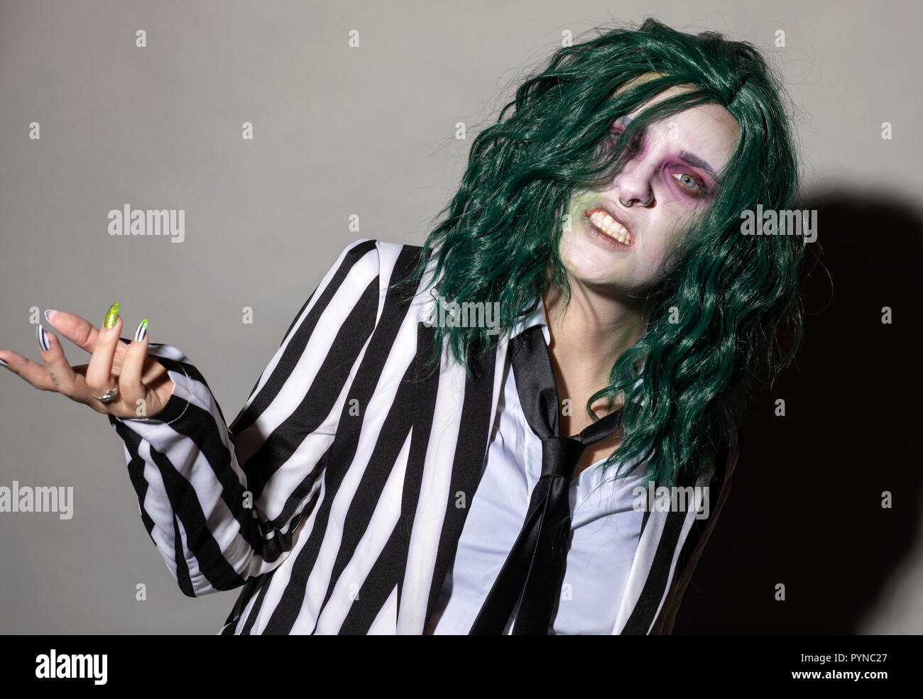 Eine junge Frau kleidet sich für Halloween im Nadelstreifenanzug und grüne Haare. Stockfoto