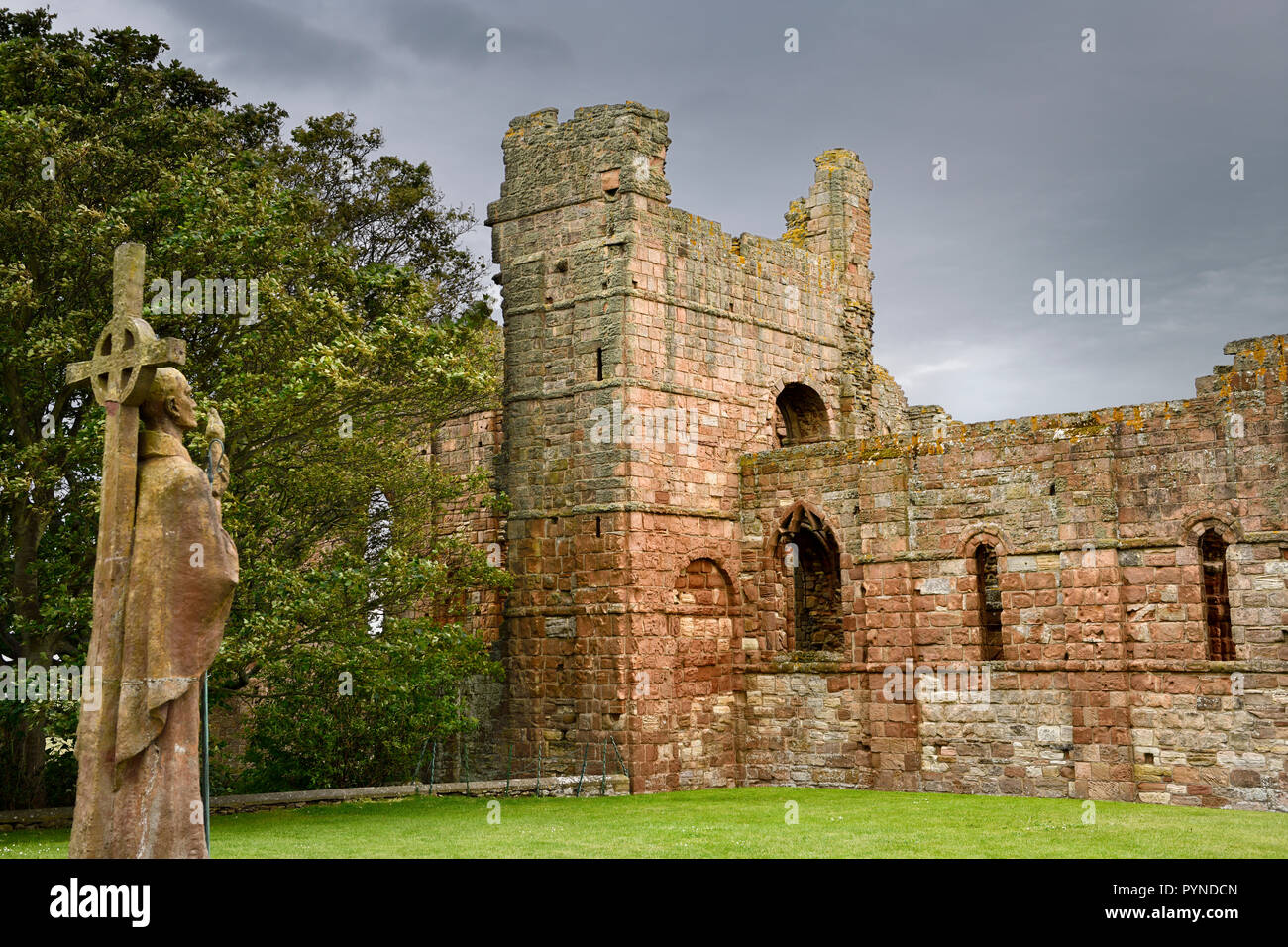 Lebensgroße Statue von St Aidan ersten Bischof von Lindisfarne mit Blick auf die Ruinen des mittelalterlichen Klosters auf der heiligen Insel von Lindisfarne England Großbritannien Stockfoto