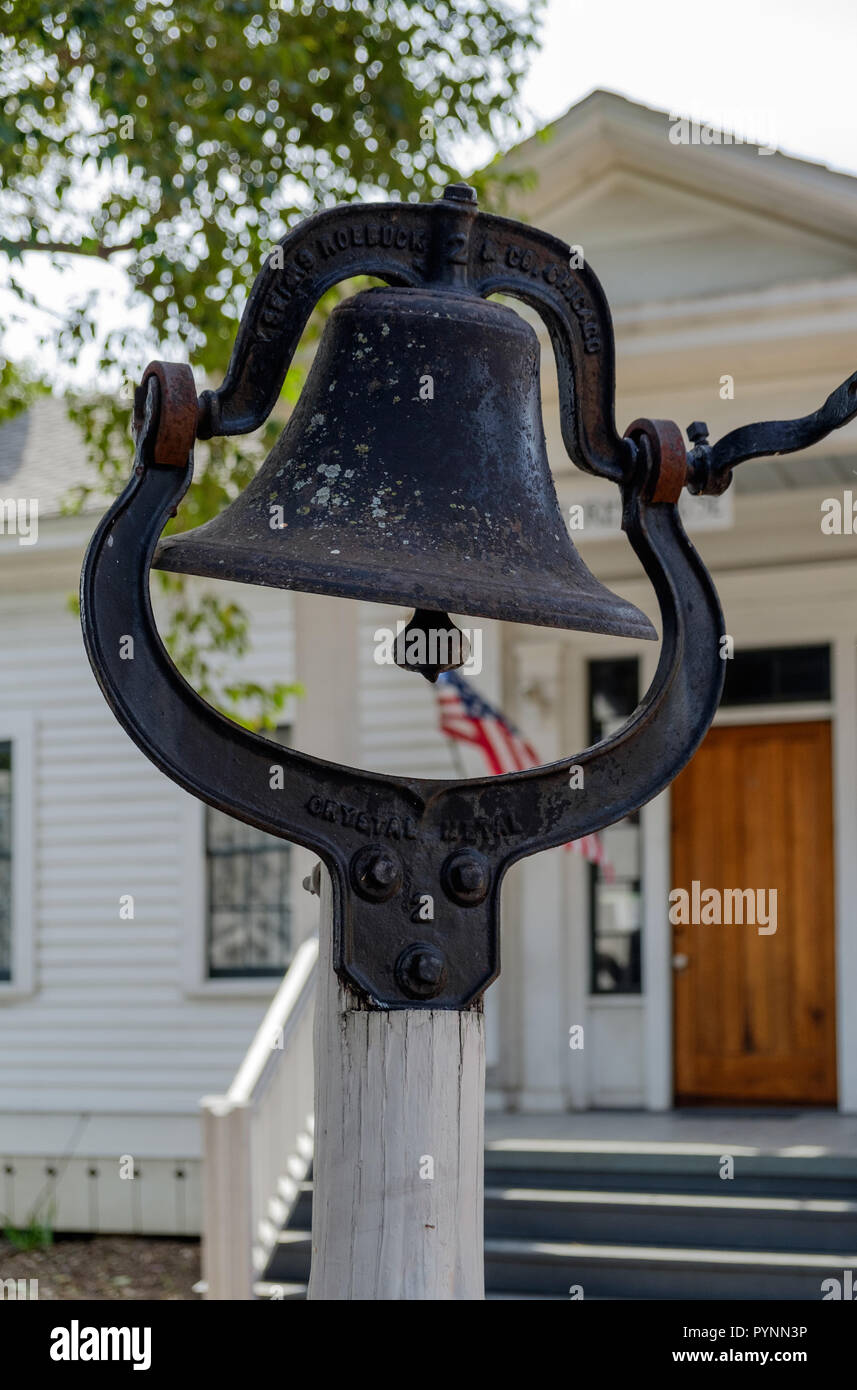 Altes Eisen Schulglocke auf weißen Pole außerhalb Replik von Wilmeth Schulhaus, Kastanie Square historische Dorf, McKinney, Texas. Porträt. Stockfoto