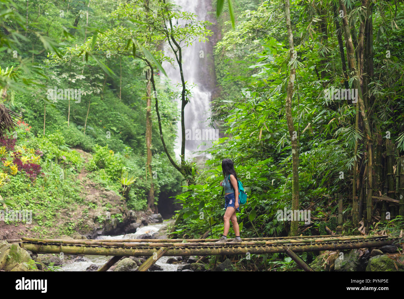 Touristische Frau Bambus Überqueren einer Brücke in der Nähe des Red Coral Munduk Wasserfall im Dschungel, Bali, Indonesien Stockfoto