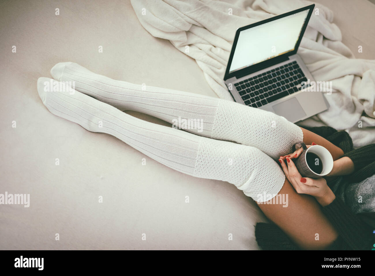 Nahaufnahme von den Beinen der jungen Frau auf dem Bett zu sitzen mit Laptop und eine Tasse Kaffee in der Hand. Stockfoto