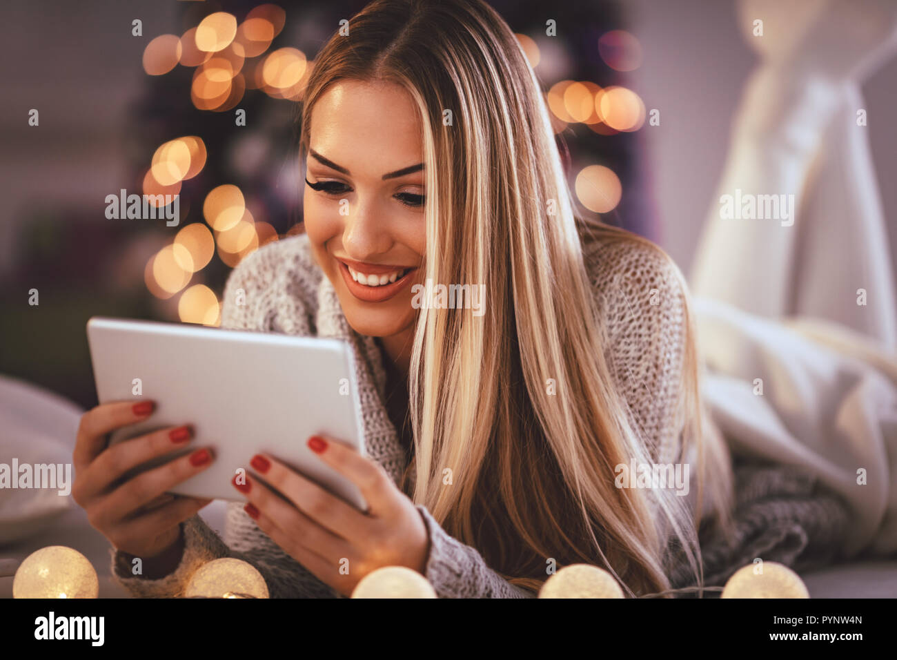 Nette junge lächelnde Frau mit Tablet und gerne während gemütliche Weihnachten Urlaub zu Hause ein Lächeln auf den Lippen. Stockfoto