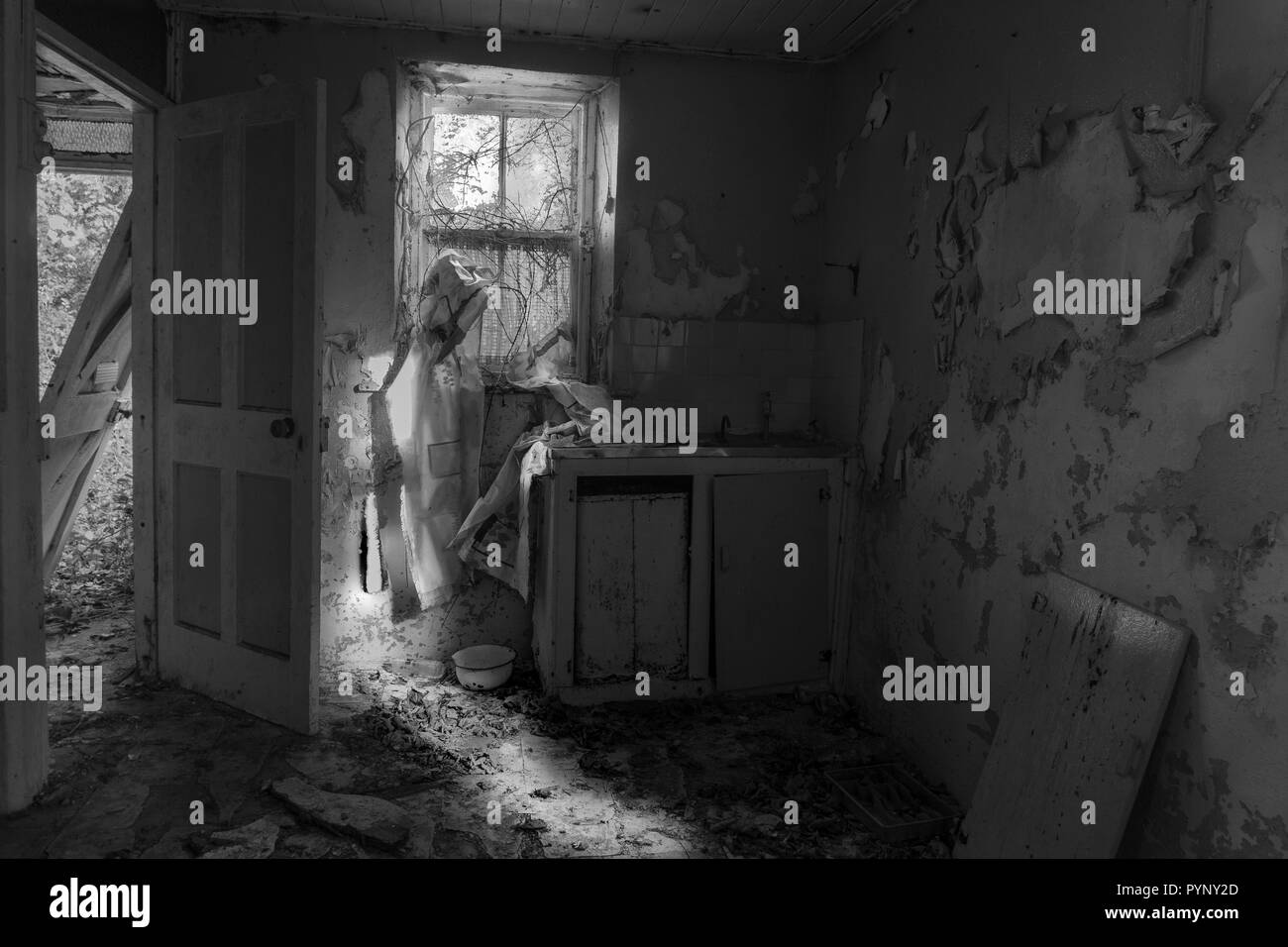 Küche, verfallenen Hütte, die Farbe blätterte ab, Spüle mit alten Schürze am Fenster, Schüssel auf dem Boden sind, Tür aus Scharniere auf der einen Seite lehnen, Schwarz + Weiß Stockfoto