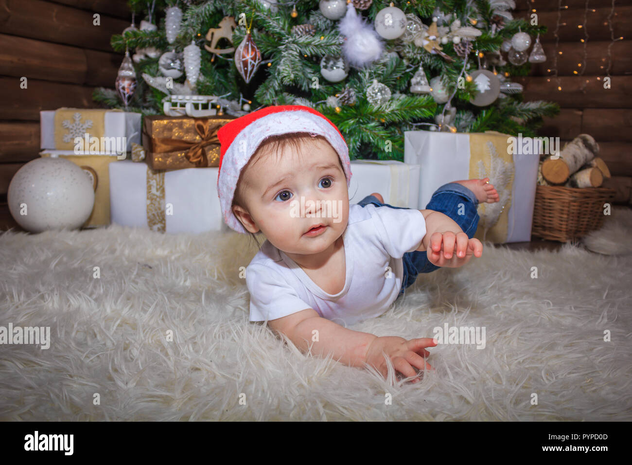 Baby in elf Kostüm spielen mit alten hölzernen Zug und Stofftier Bären unter den Weihnachtsbaum, vintage. Das Baby in die Gap liegt unter dem Baum und sm Stockfoto