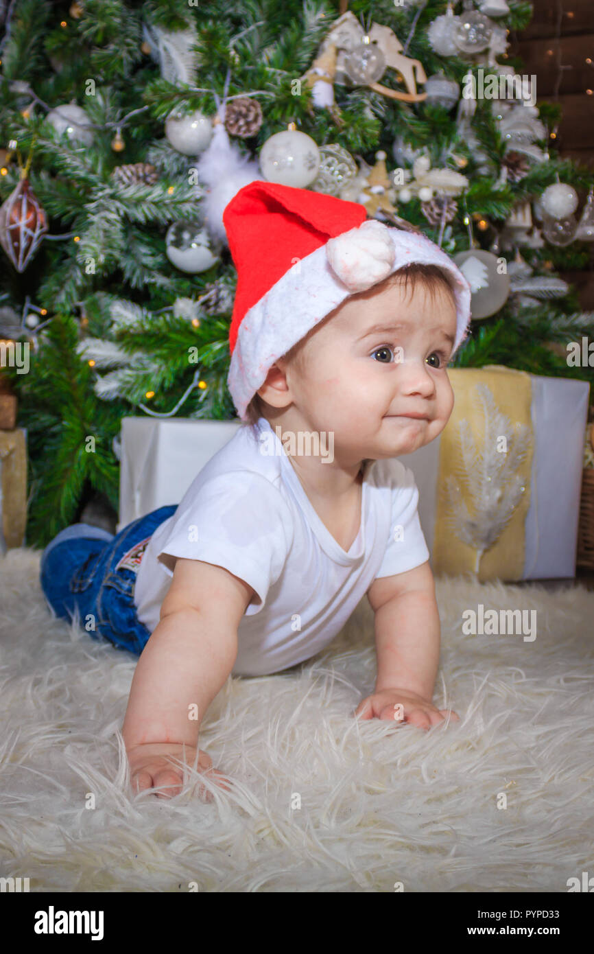 Baby in elf Kostüm spielen mit alten hölzernen Zug und Stofftier Bären unter den Weihnachtsbaum, vintage. Das Baby in die Gap liegt unter dem Baum und sm Stockfoto